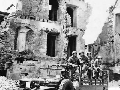Troops and Dodge WC63 truck amid ruins of Trevieres 1944