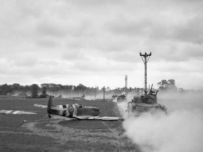 Sherman tanks move up past a crash landed Spitfire, for an attack on Tilly-sur-Seulles, Normandy 17 June 1944