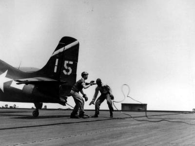 Flight deck crewmen remove the arresting wire from the tailhook of an FM-2