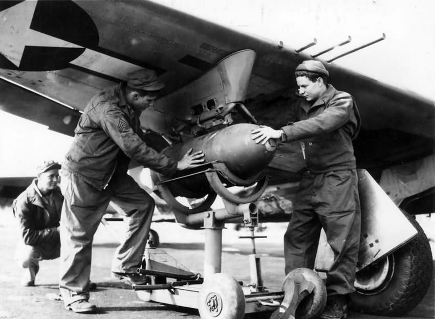 Ground crew affix a 500 lb bomb to the underside of wing of a P-47 56th FG 1944