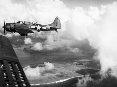 SBD-5 white 16 of VB-16 flies over ships of the invasion force to strike Japanese installations ashore on D-Day for the invasion of Saipan on June 15, 1944