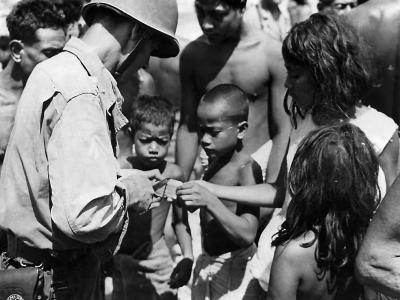 US officer of the 165th Infantry cuts up a piece of canned meat for hungry children