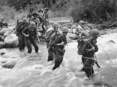 US troops and native porters cross stream in New Guinea 1942