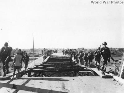 Infantrymen crossing damaged Calmay Bridge on Luzon