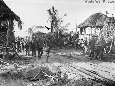 Troops move thru ruins of native village on Luzon 1945